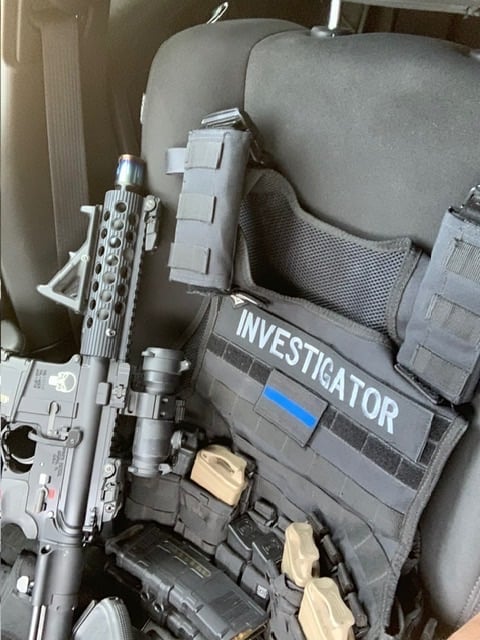 Tactical gear and rifle with INVESTIGATOR vest loaded in vehicle seat with ammunition magazines and equipment